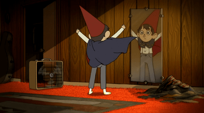 A screencap from episode nine showing Wirt after he's put on his signature outfit. He's looking in the mirror with a fan on to make his cape blow, and he's throwing his arms in the air.