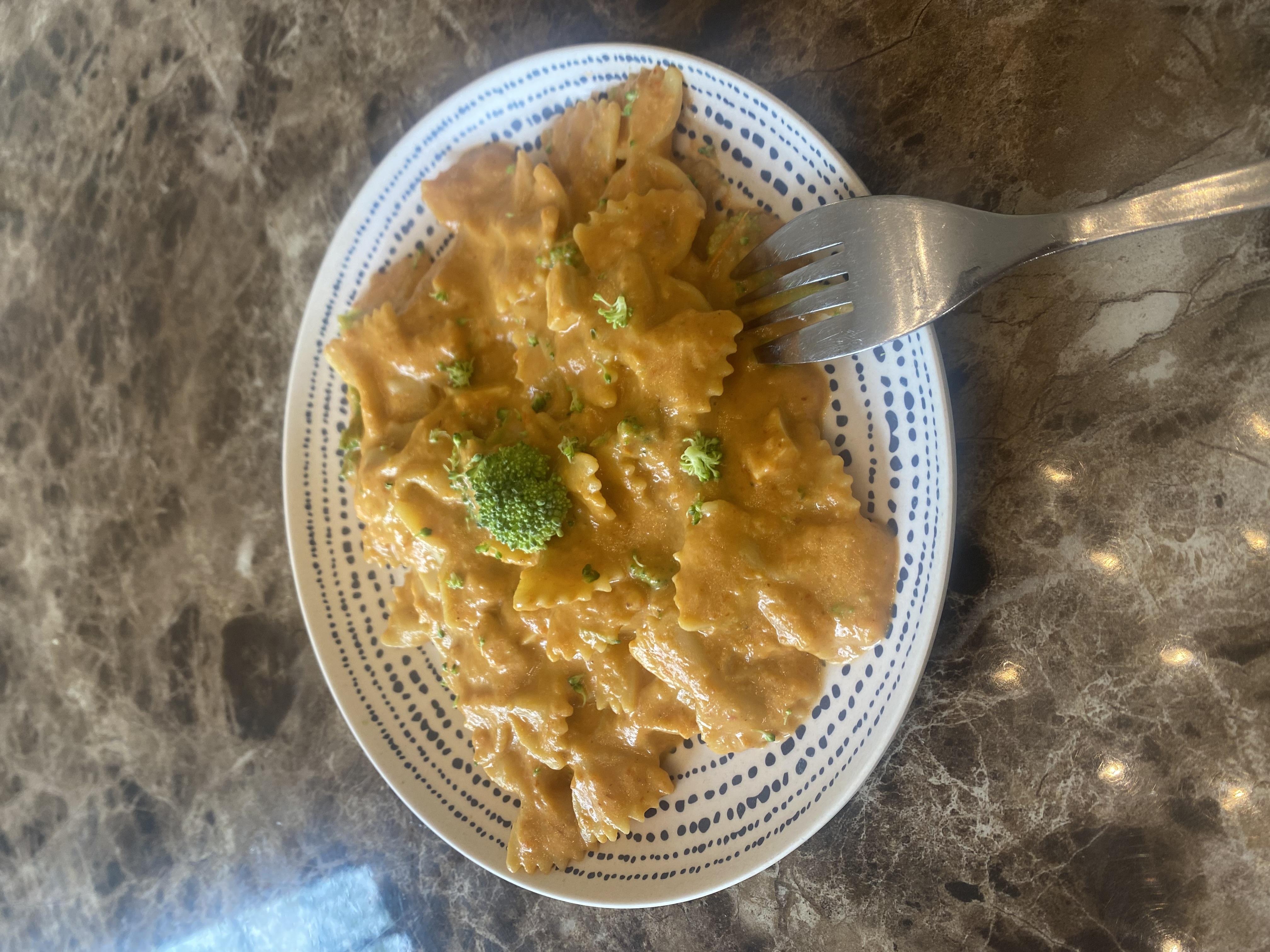 A plate of bowtie pasta in an orange-ish sauce mixed in with broccoli.