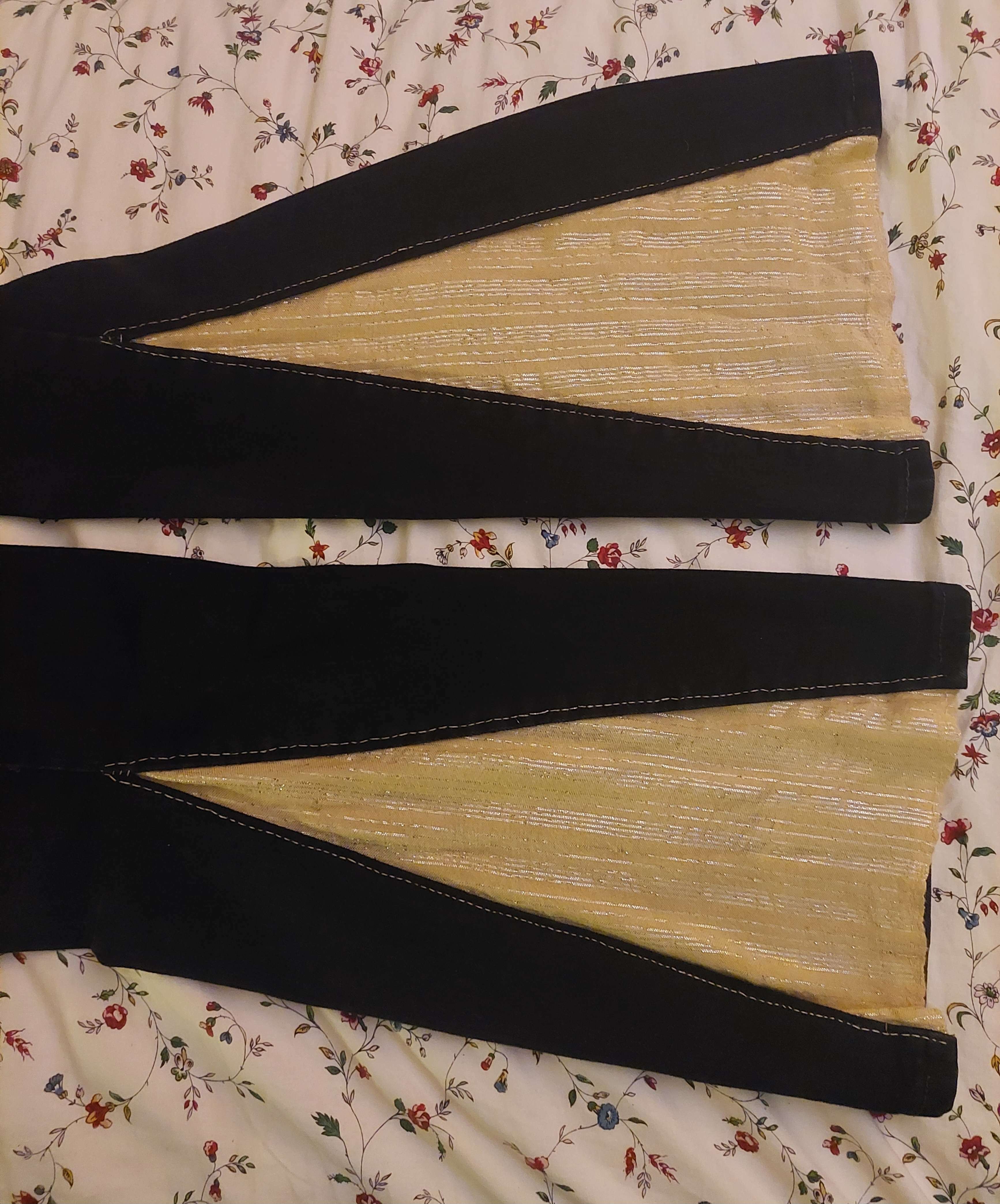 two black jean pantlegs with their outer seam split from the knee down with a sparkly yellow flare sewn in with gold thread.