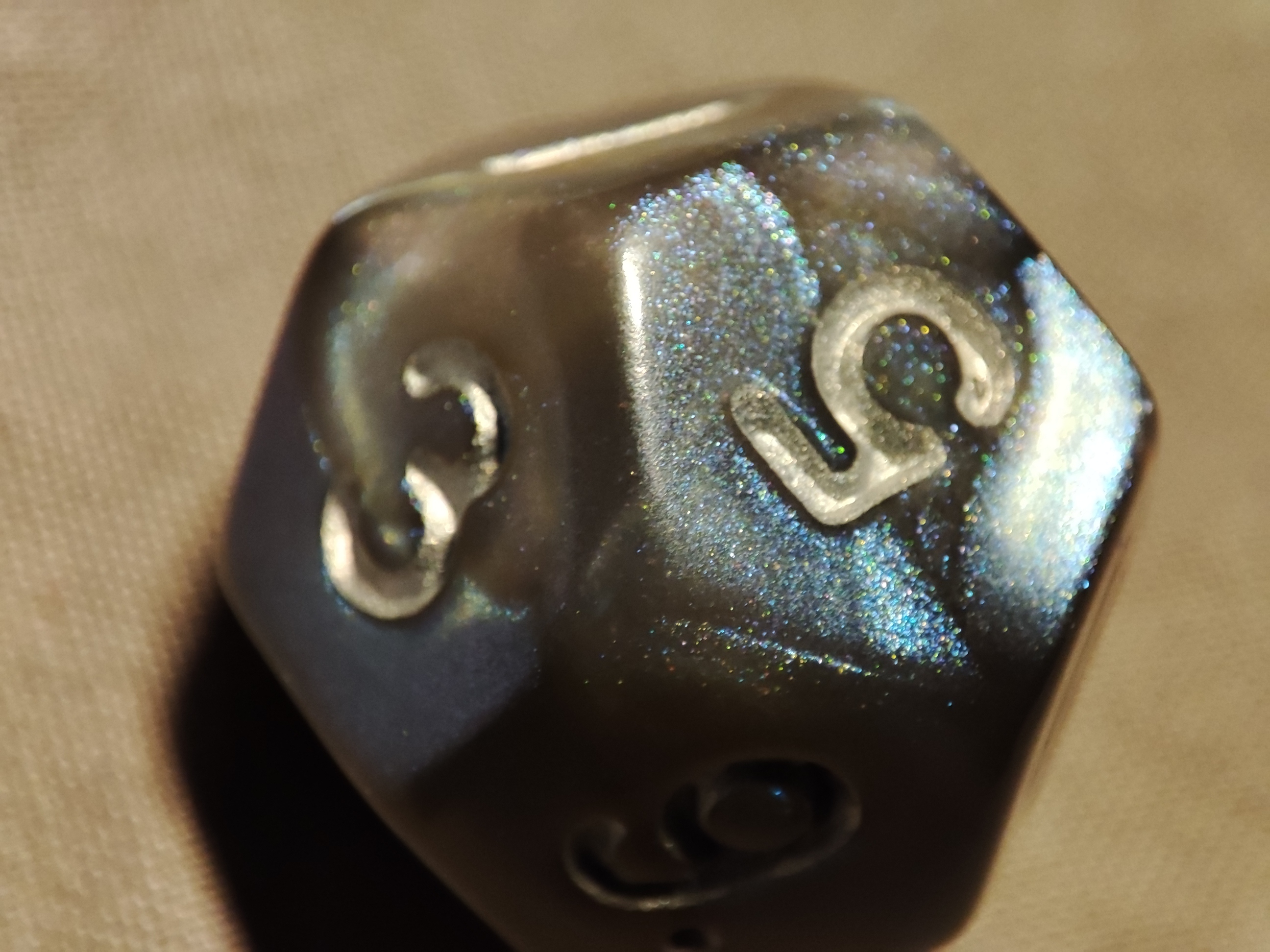 A grey die with rainbow glitter, the die has 12 sides and the 5 is facing up