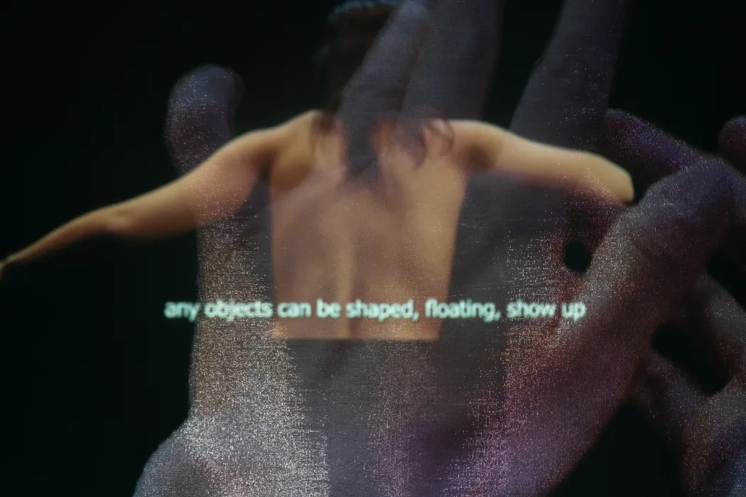 in front of one projection video of a person, there is big hands projected on the half transparent screen